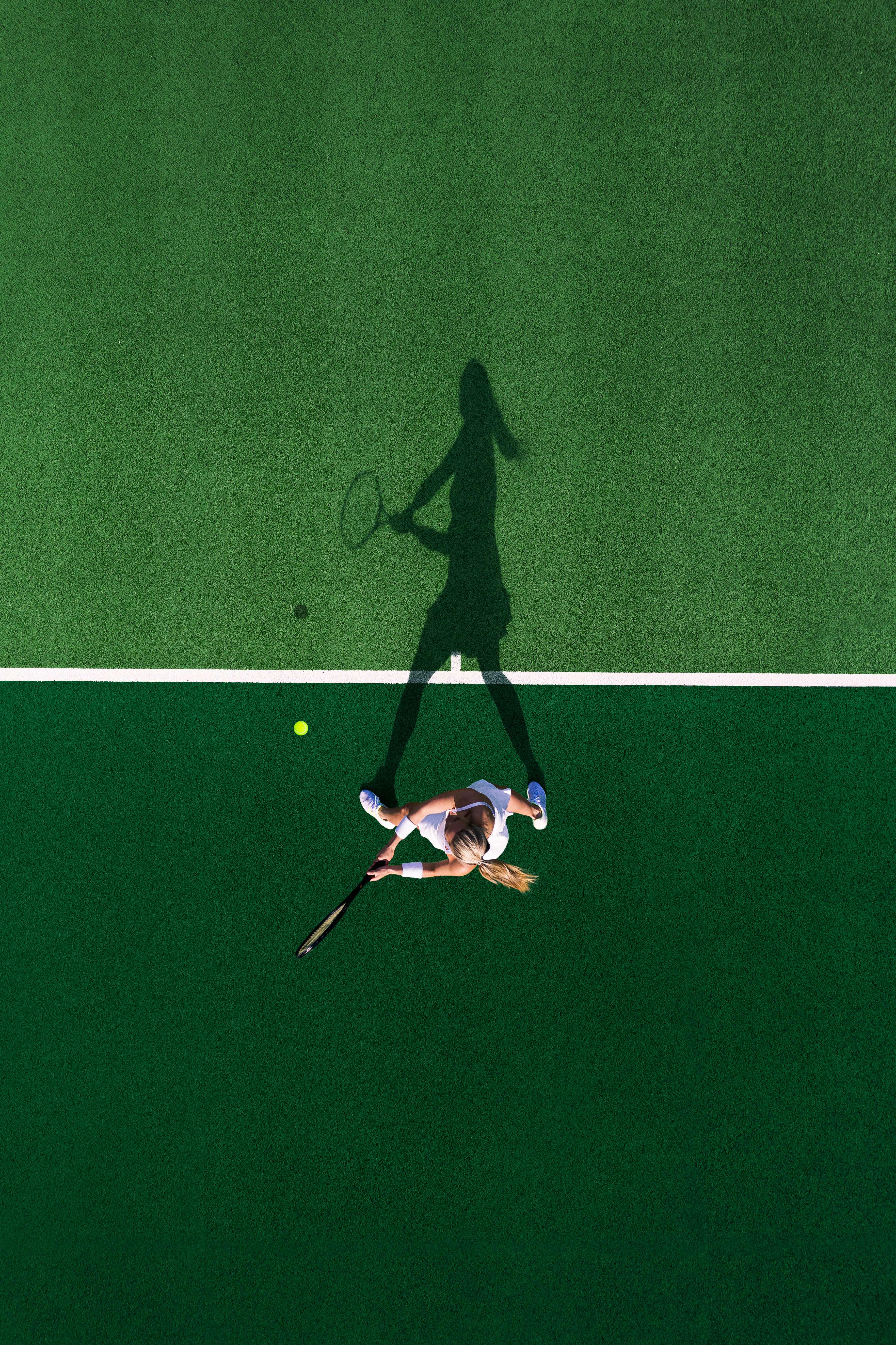 Aerial view of a tennis player preparing to hit the ball on a green court.