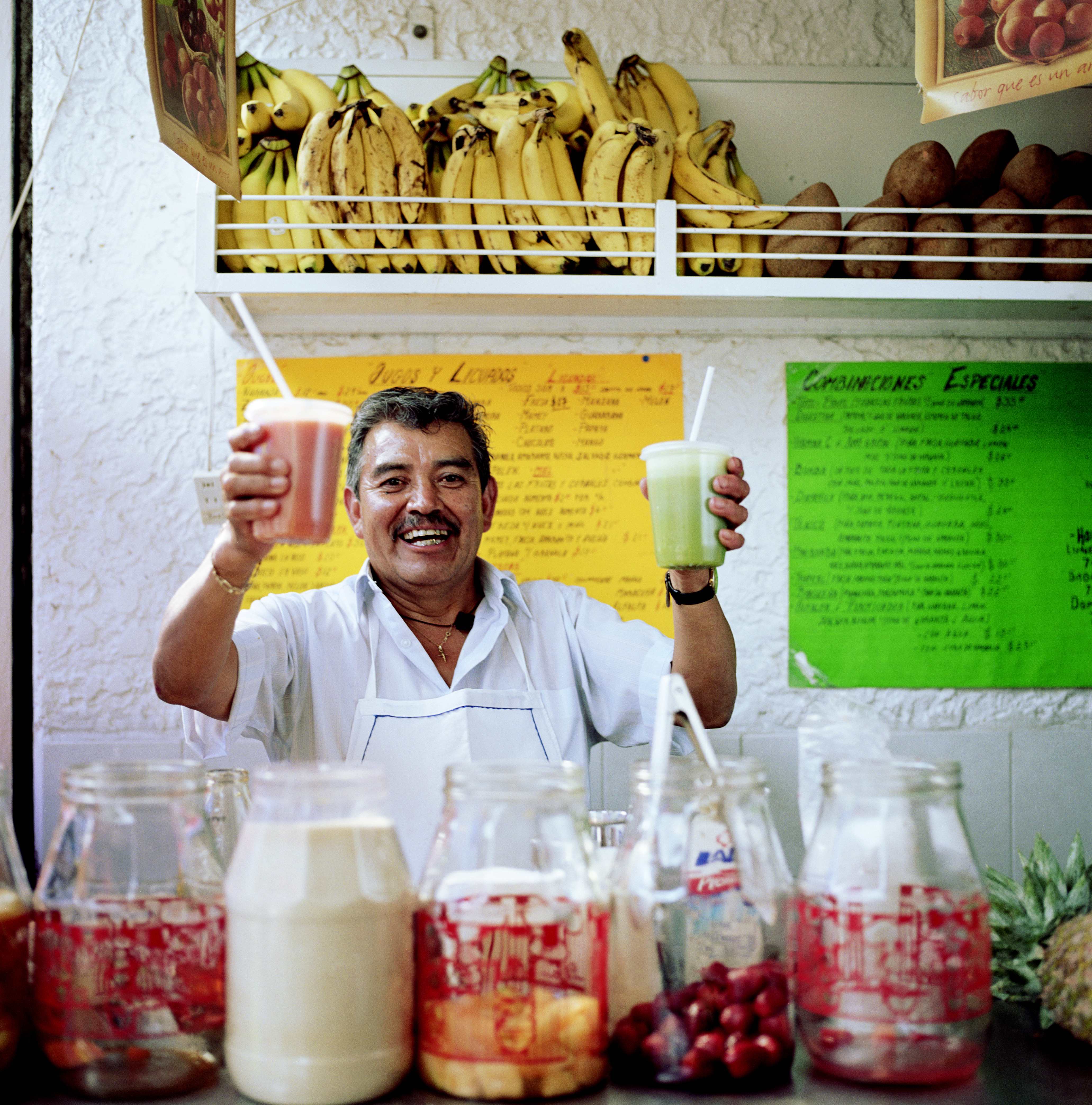 Man at a juice stand in Mexico City, smiling and holding up two fresh drinks.