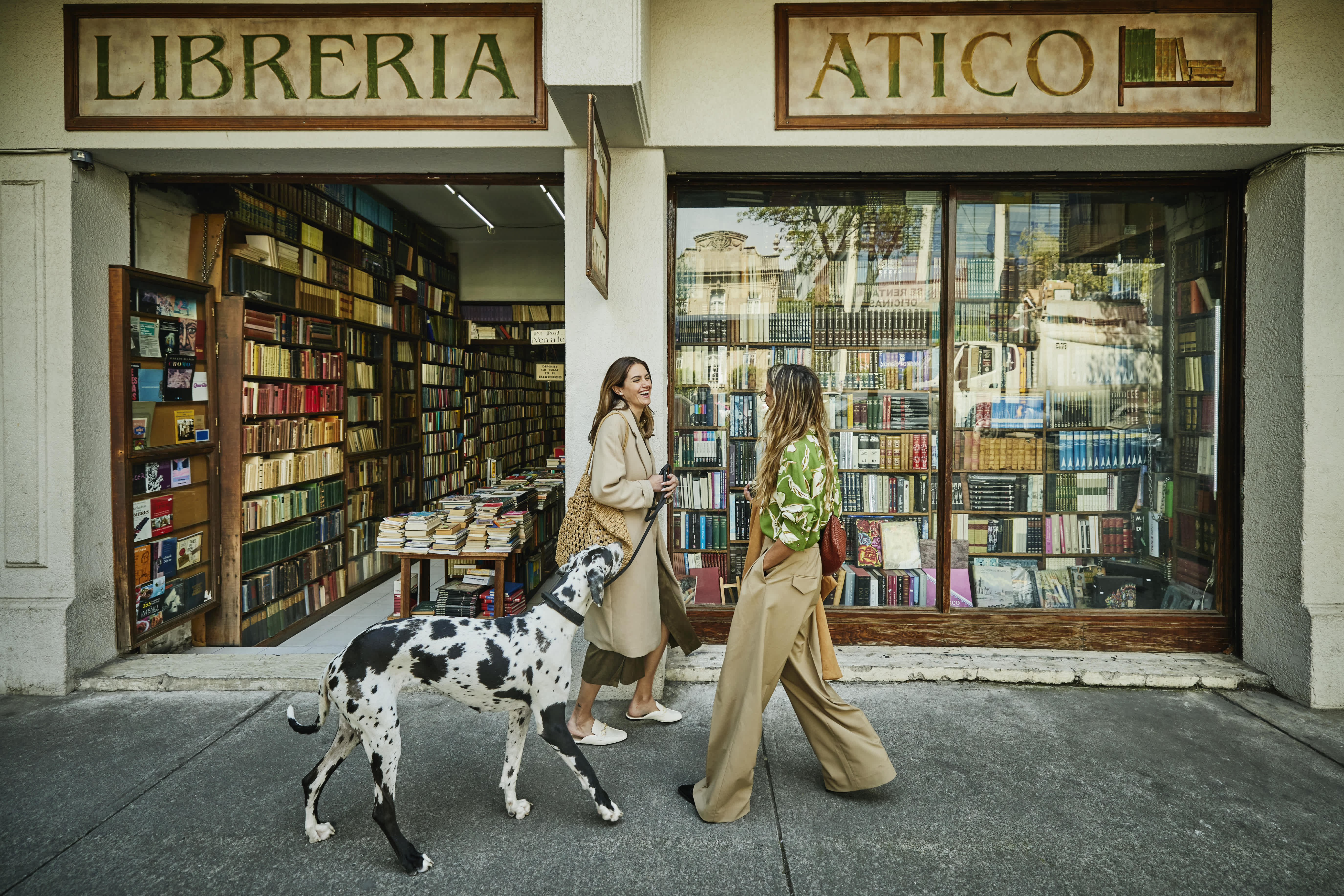 Two women walking a dog in front of a bookstore in Mexico City.