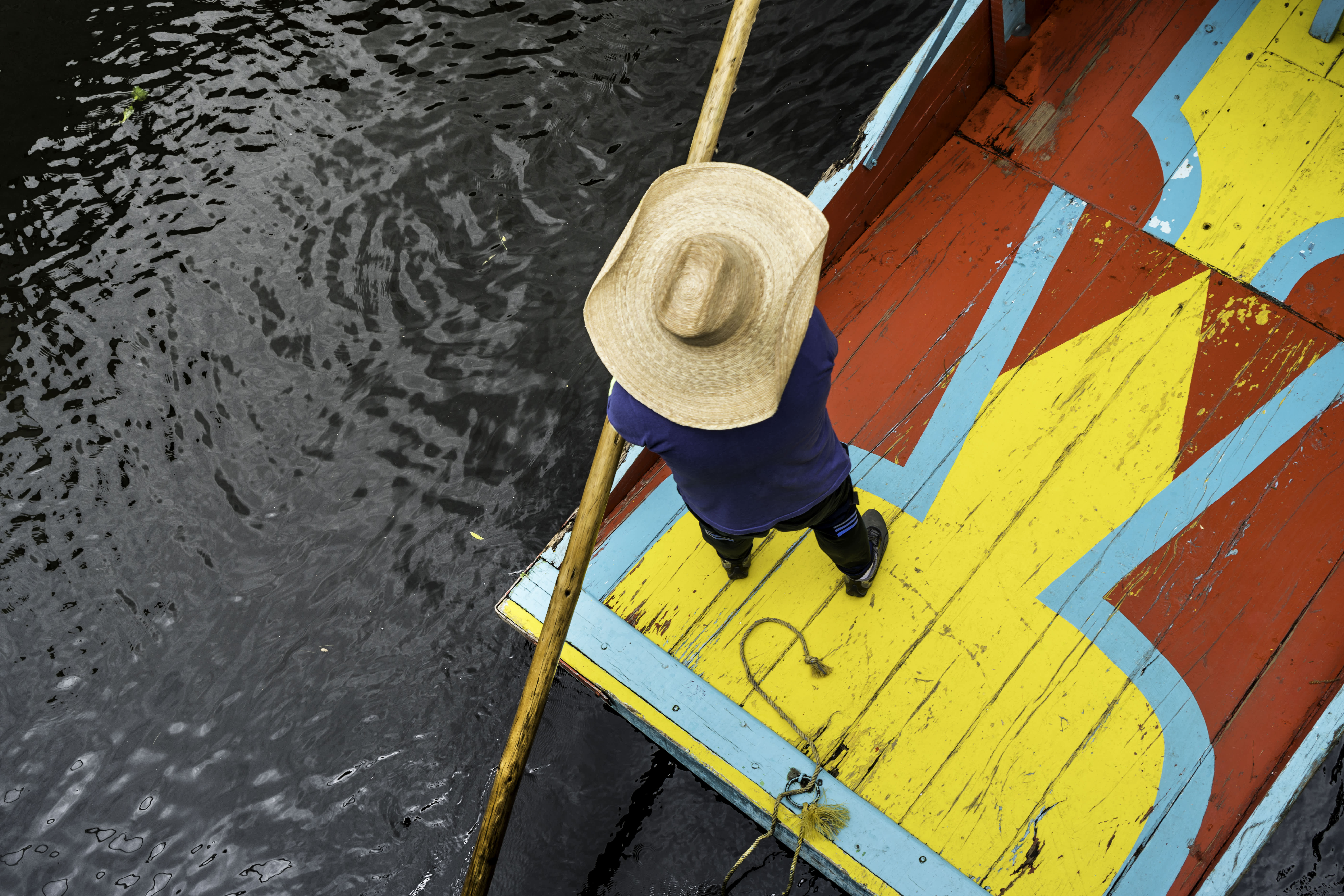 Man steering a colorful boat along the water in Xochimilco, Mexico.