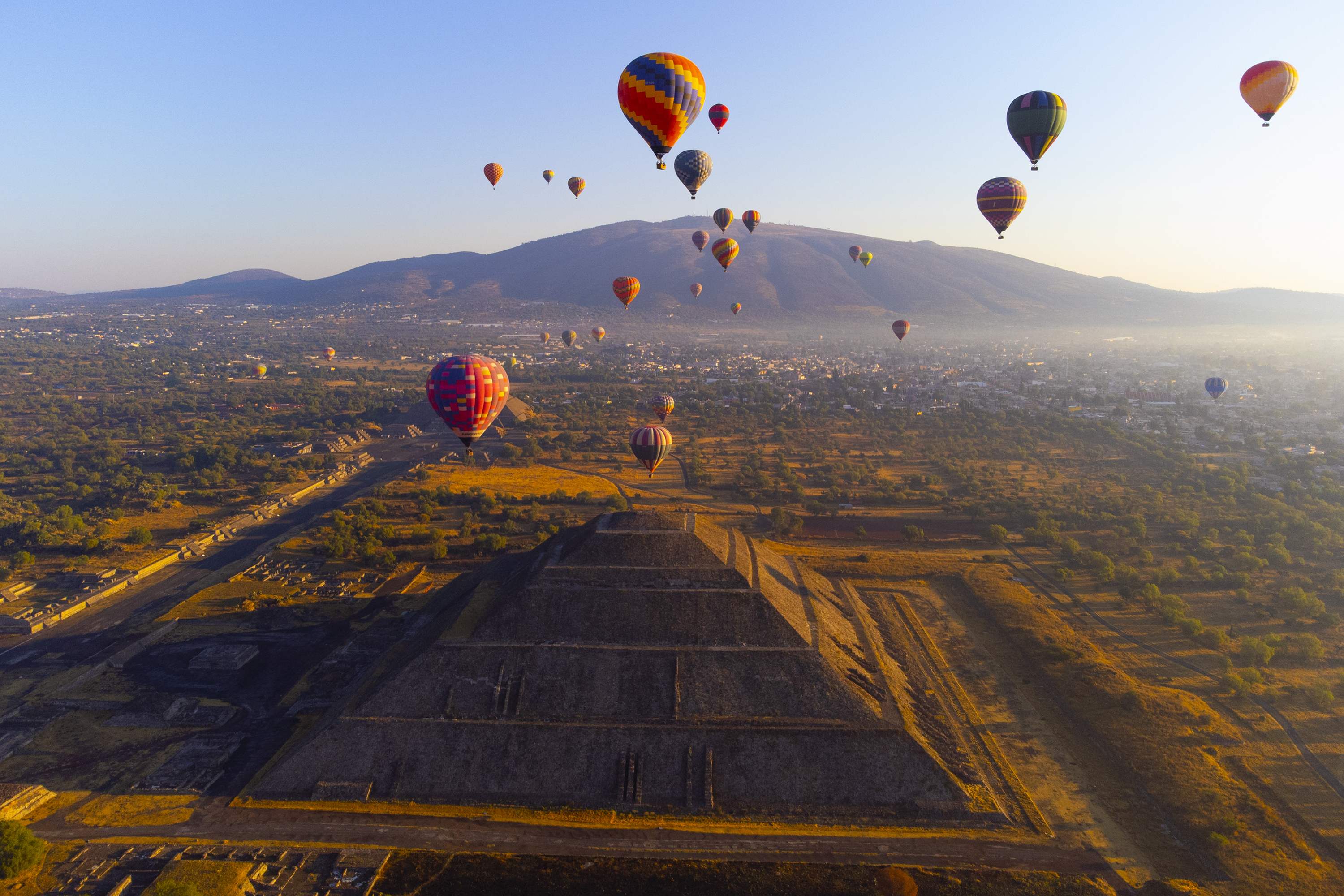 Hot air balloons floating over the Pyramid of the Sun in Teotihuacan, Mexico, at sunrise.