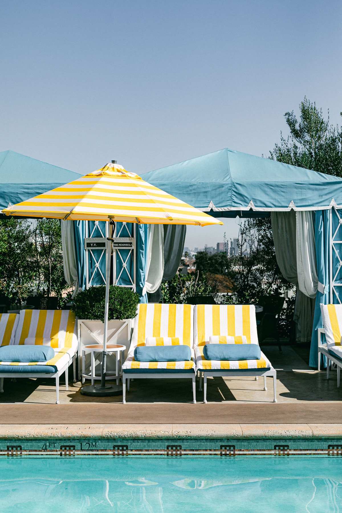 Poolside loungers with yellow and white striped towels under a yellow umbrella at The Peninsula Beverly Hills.