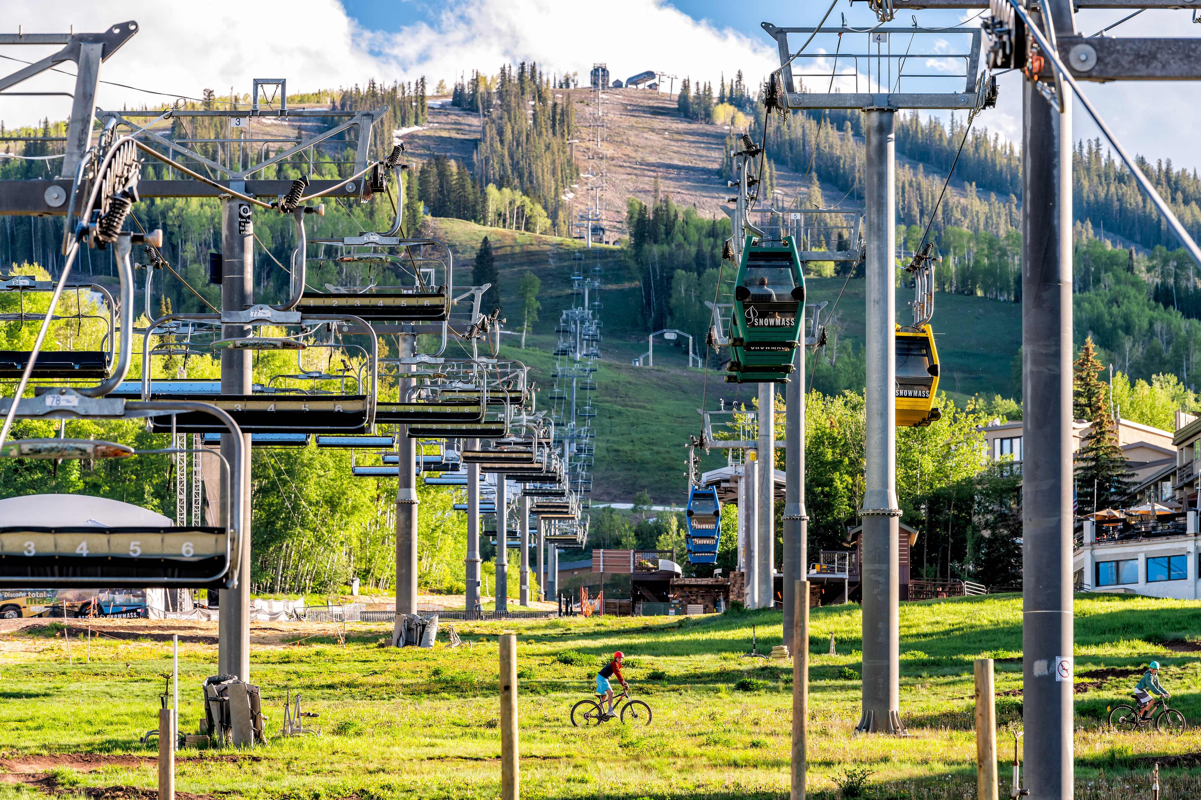 Bicyclists riding through a green summer landscape under the Snowmass ski lifts in Snowmass, Colorado.