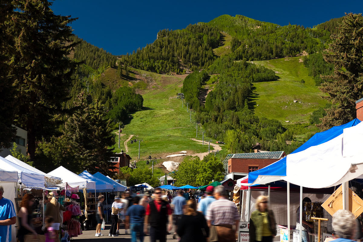 Visitors browsing stalls at the Aspen Saturday Market with a backdrop of lush green mountains in Aspen, Colorado.