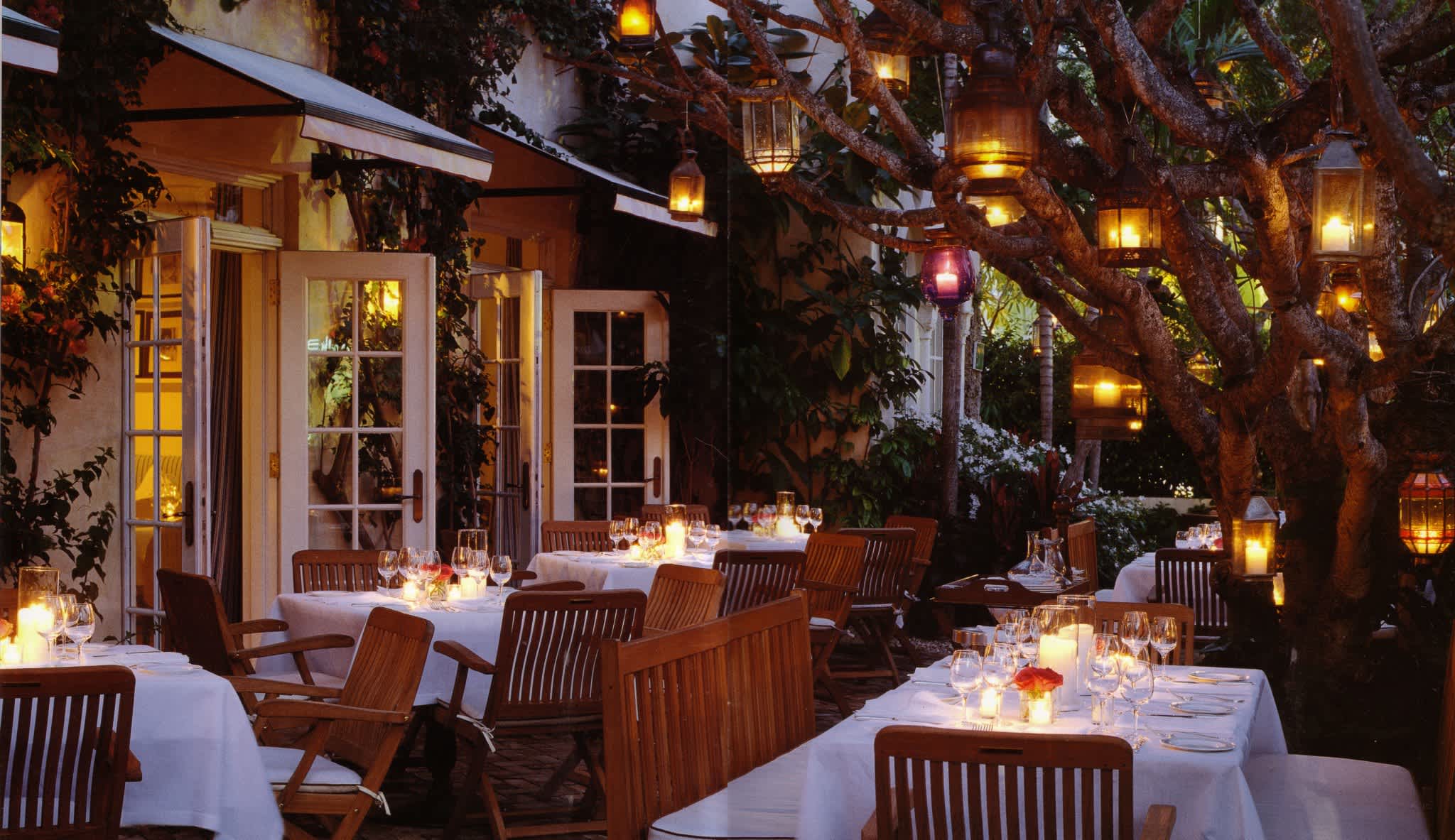 Cozy outdoor dining area at Casa Tua Aspen, decorated with candlelit tables and lanterns hanging from trees, creating an intimate atmosphere.