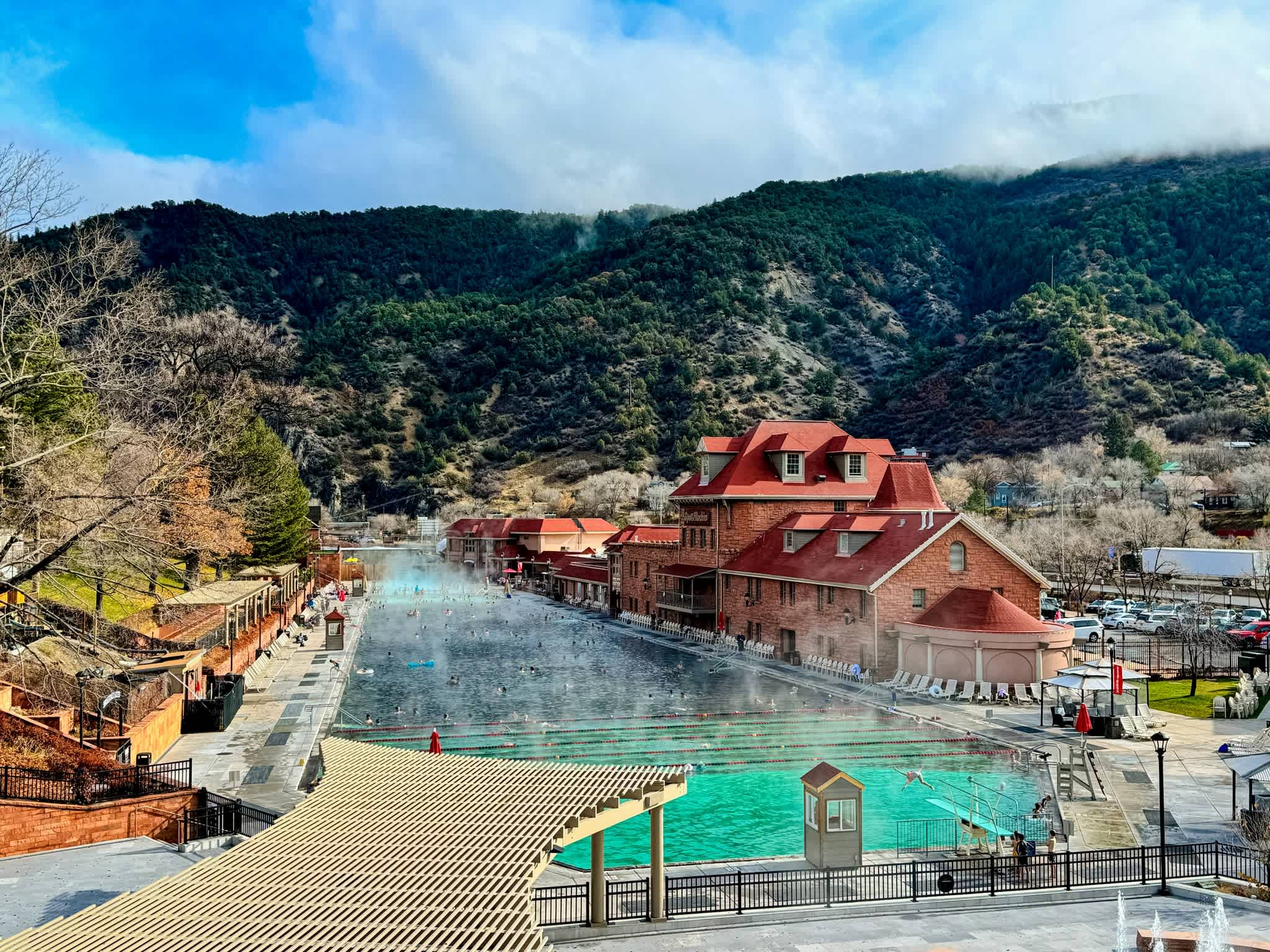 Aerial view of Glenwood Hot Springs Resort with its steaming pool set against the backdrop of forested mountains in Glenwood Springs, Colorado.