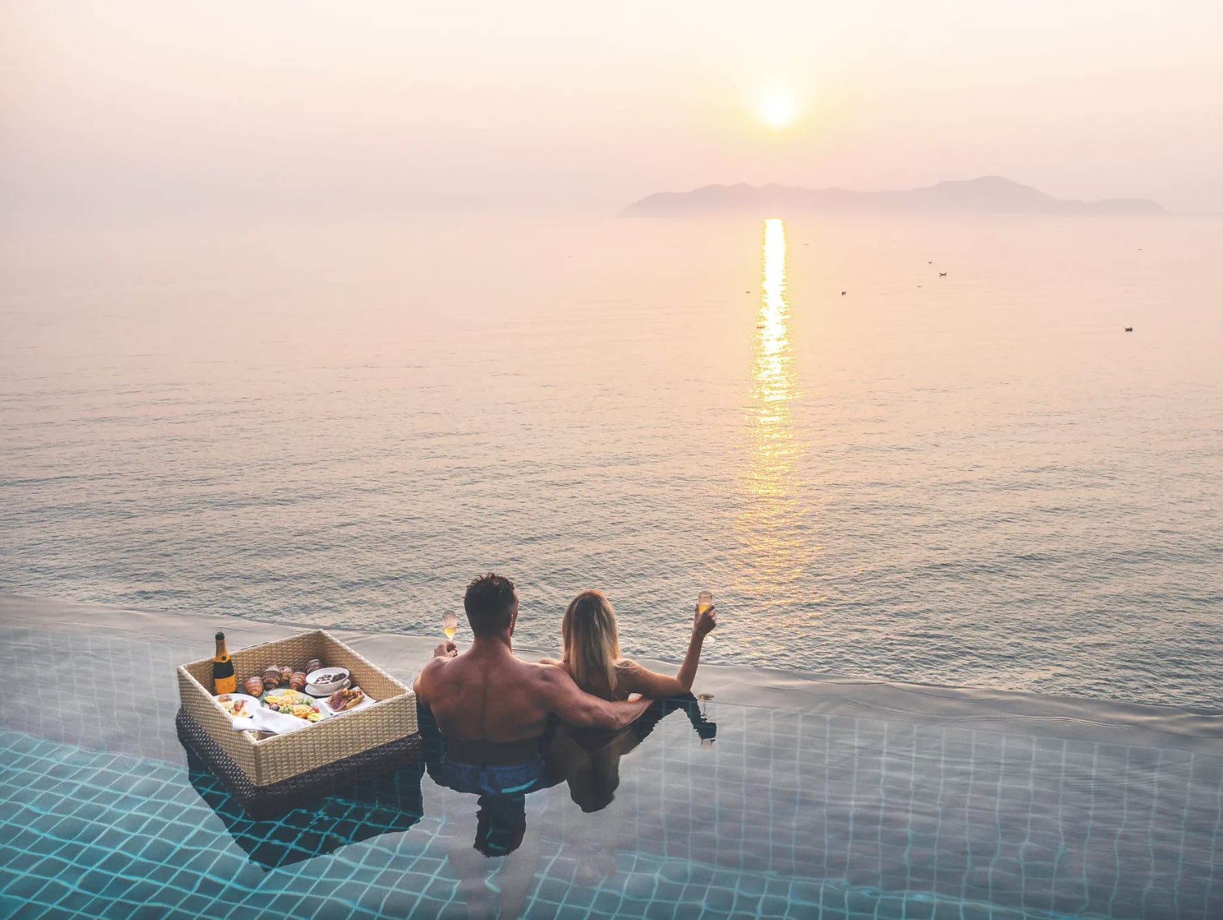 Couple enjoying a sunset view from an infinity pool with a floating breakfast in Lang Co, Vietnam.