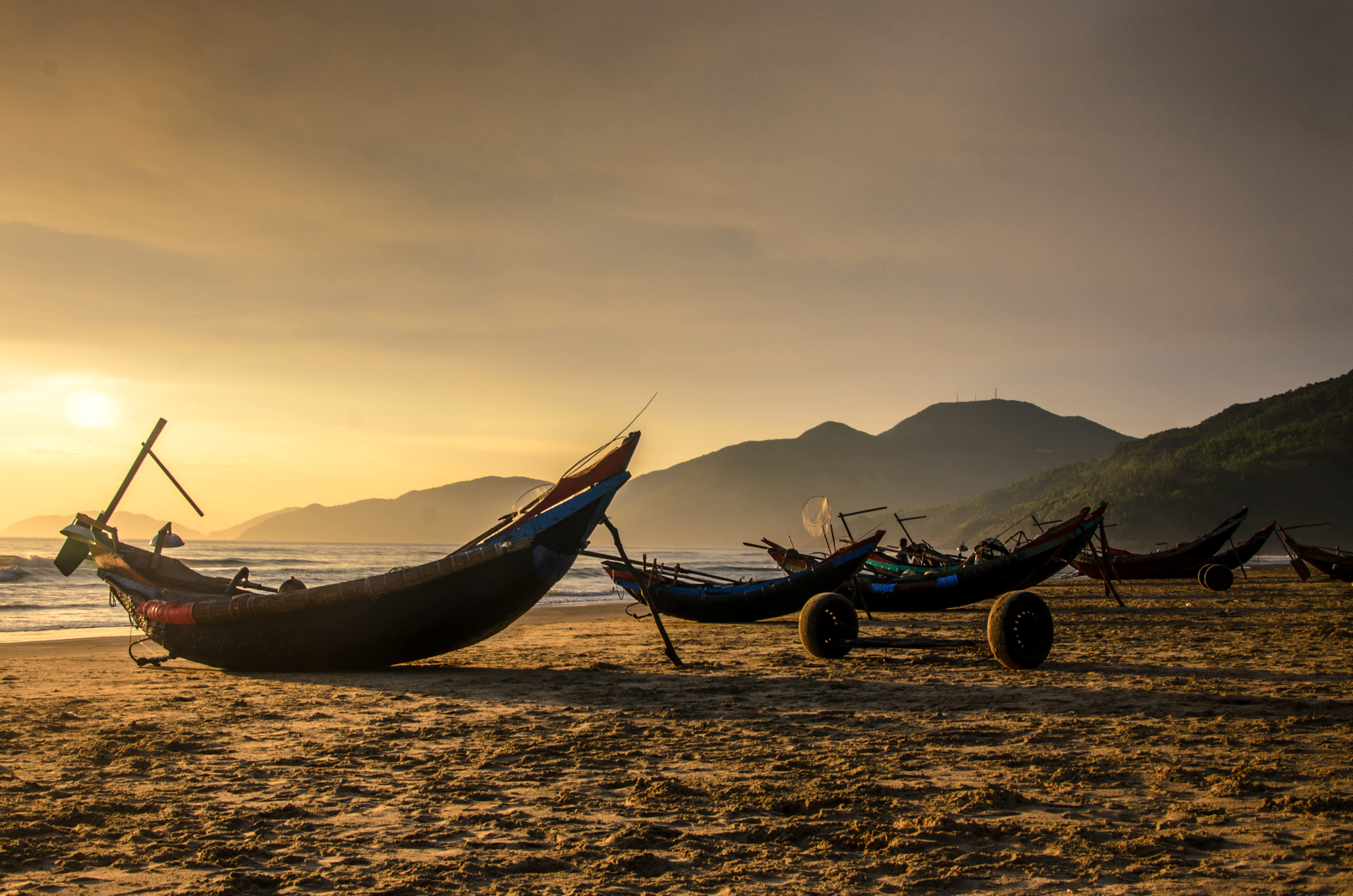 Traditional fishing boats on the sandy beach at sunrise in Lang Co, Vietnam.