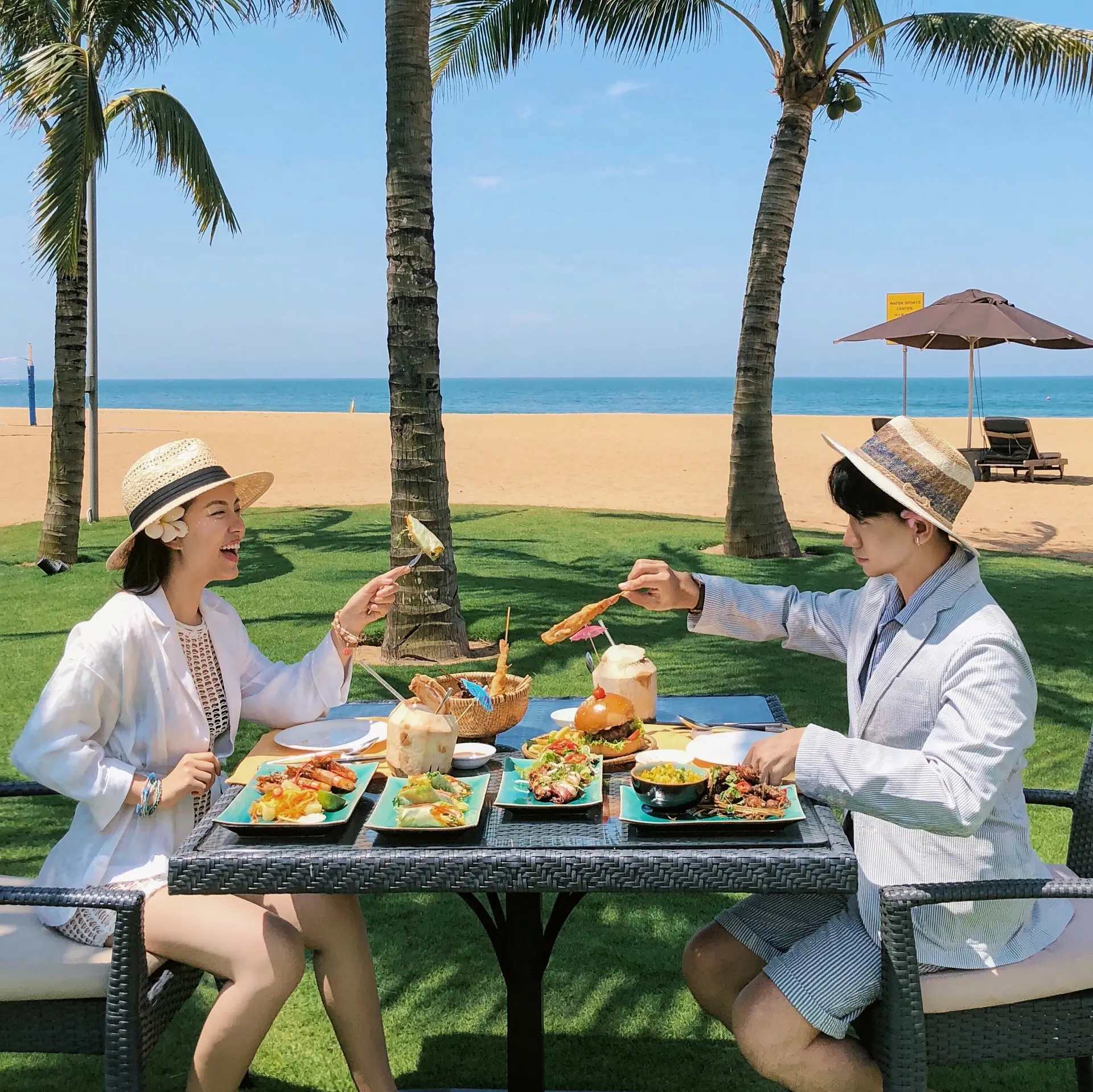 Couple enjoying a beachfront meal at Moomba Restaurant, under palm trees at Banyan Tree Lang Co, Vietnam.