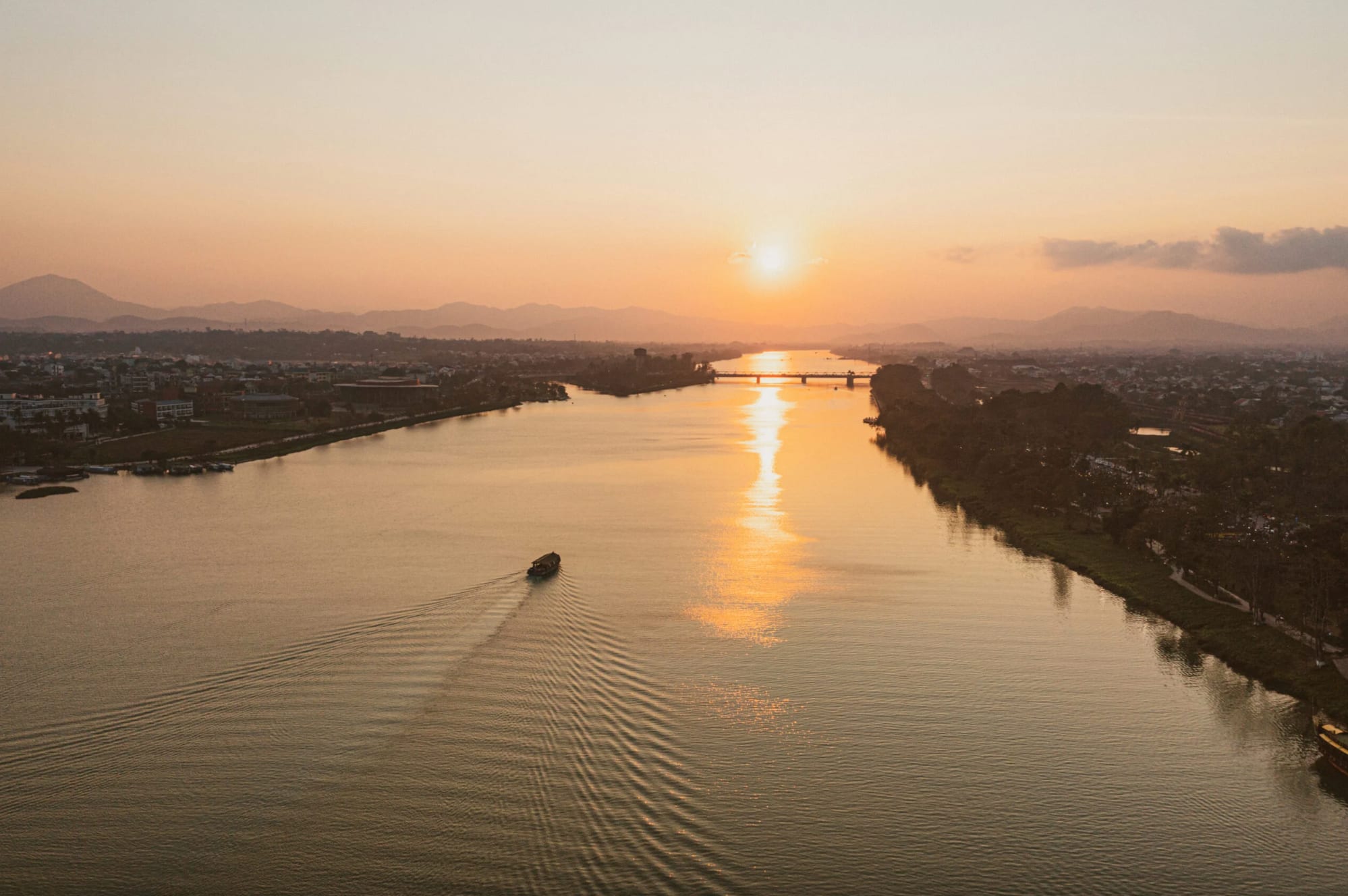 Aerial view of a river at sunset with a boat cruising and a bridge in the distance in Lang Co, Vietnam.