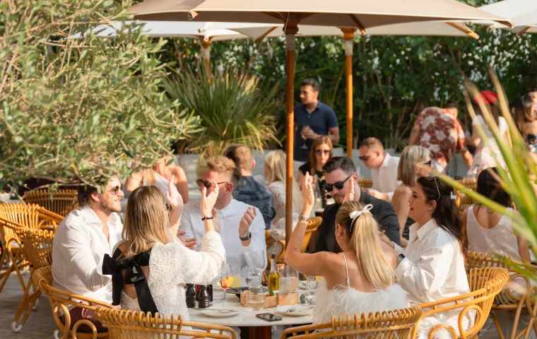 Group of people enjoying an outdoor brunch under umbrellas in a garden setting.