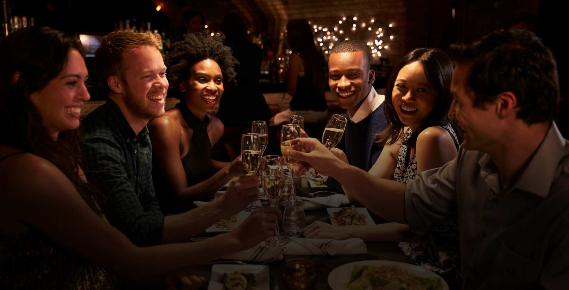 Group of friends enjoying dinner and toasting with champagne at a dimly lit restaurant.