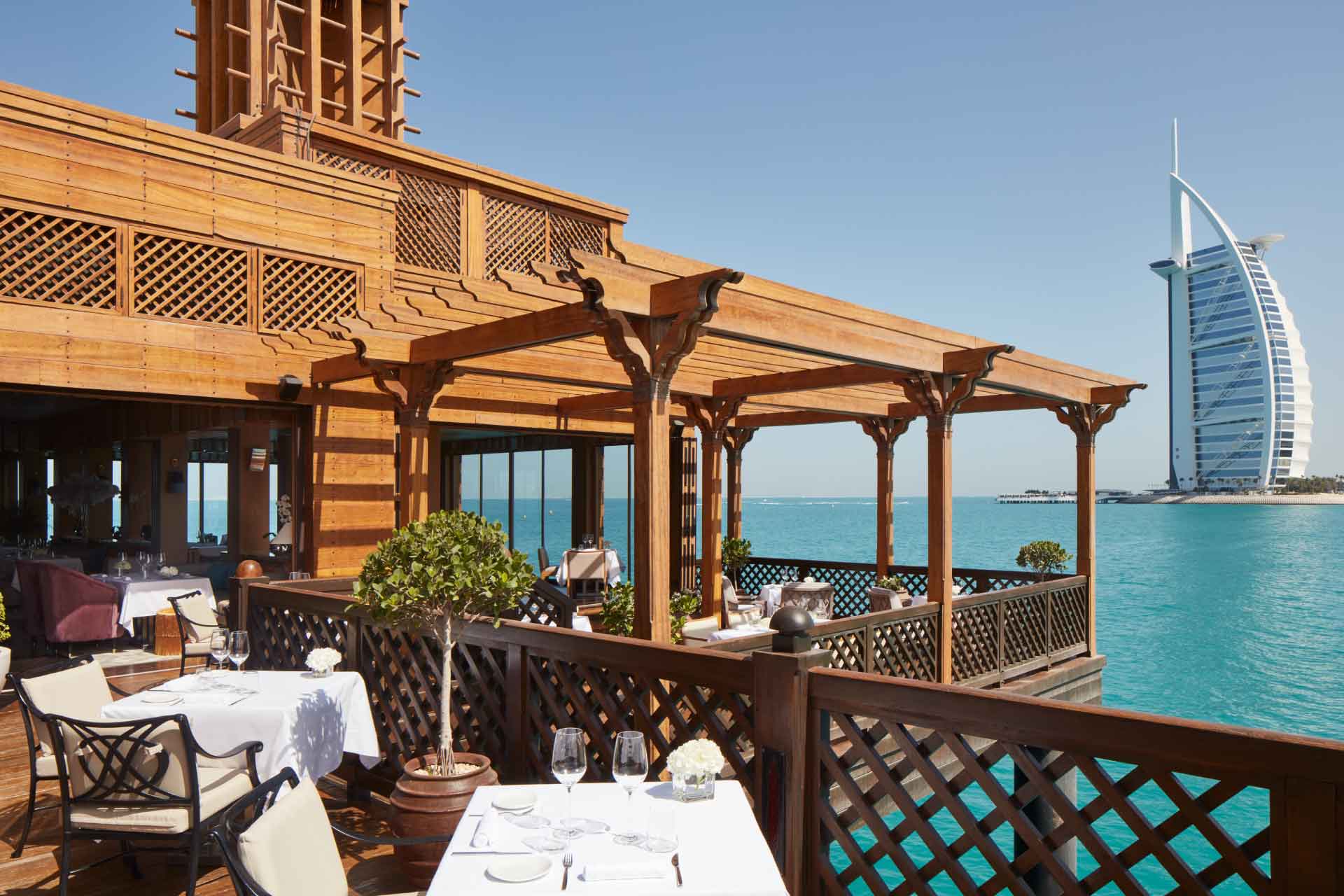 Seaside restaurant with wooden terrace overlooking the Burj Al Arab and turquoise waters in Dubai.