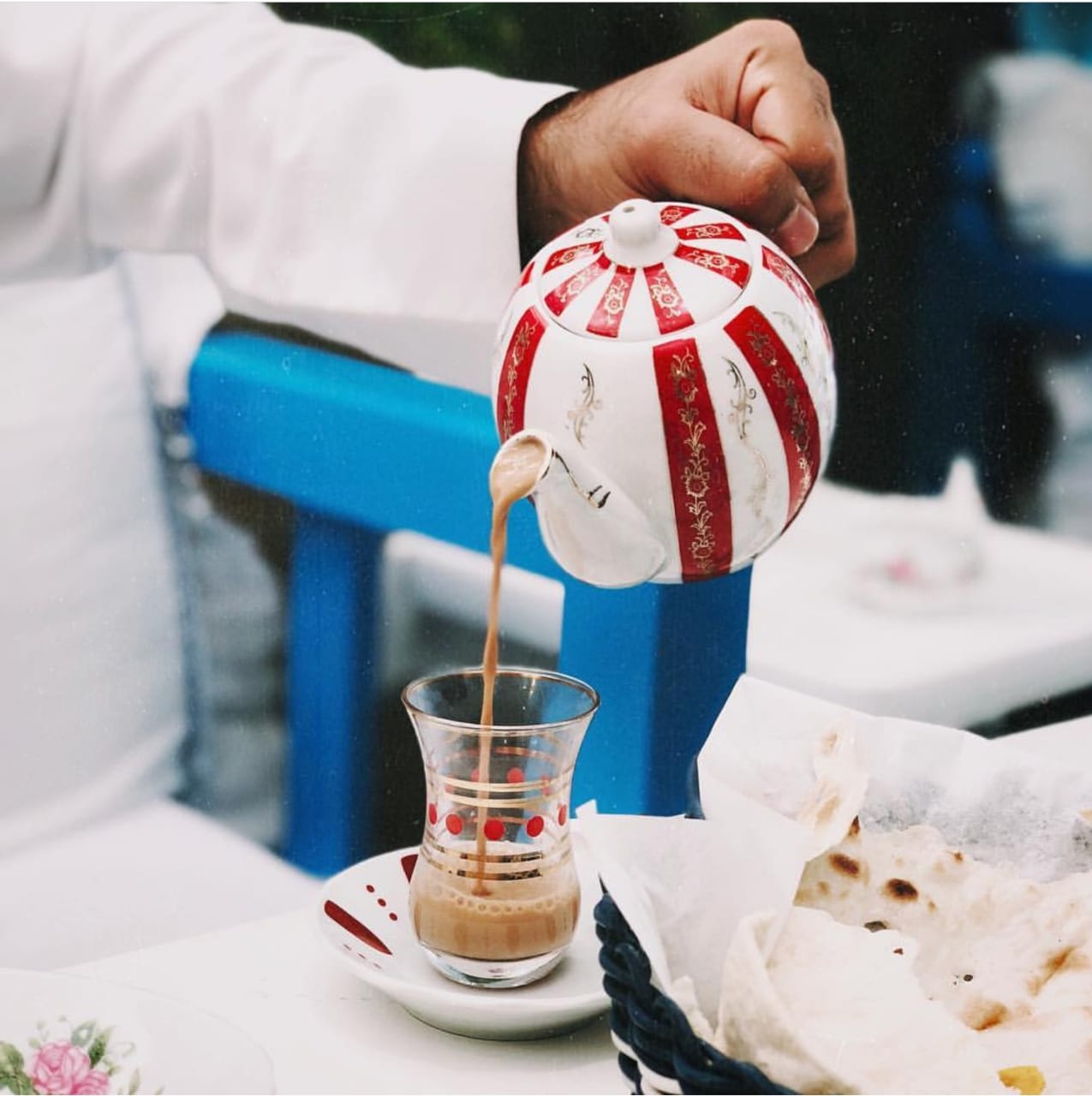 Traditional Arabic tea being poured from a decorative teapot into a small glass cup, served with flatbread on the side.