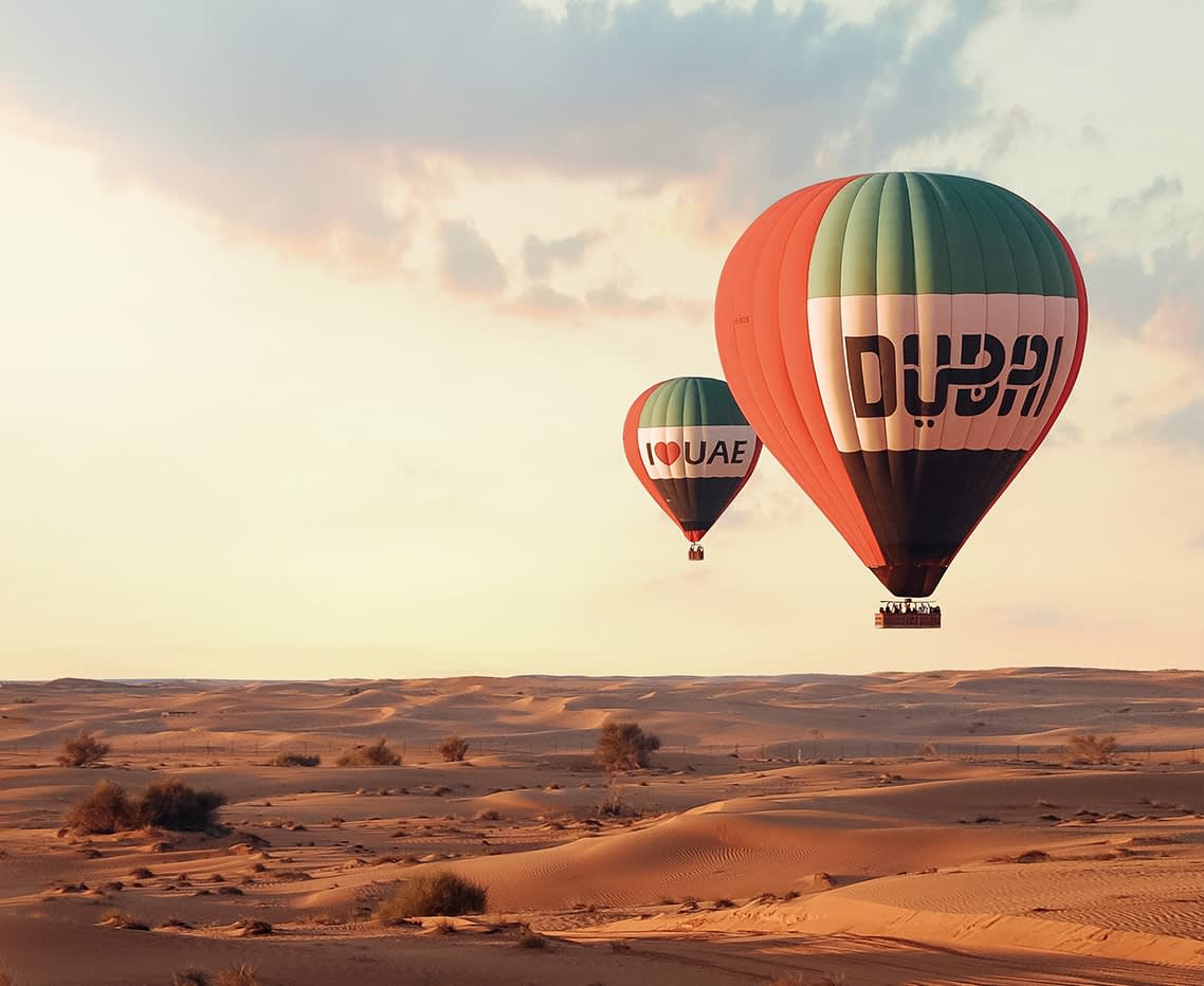Hot air balloons with "Dubai" and "I LOVE UAE" flying over the desert at sunrise or sunset.