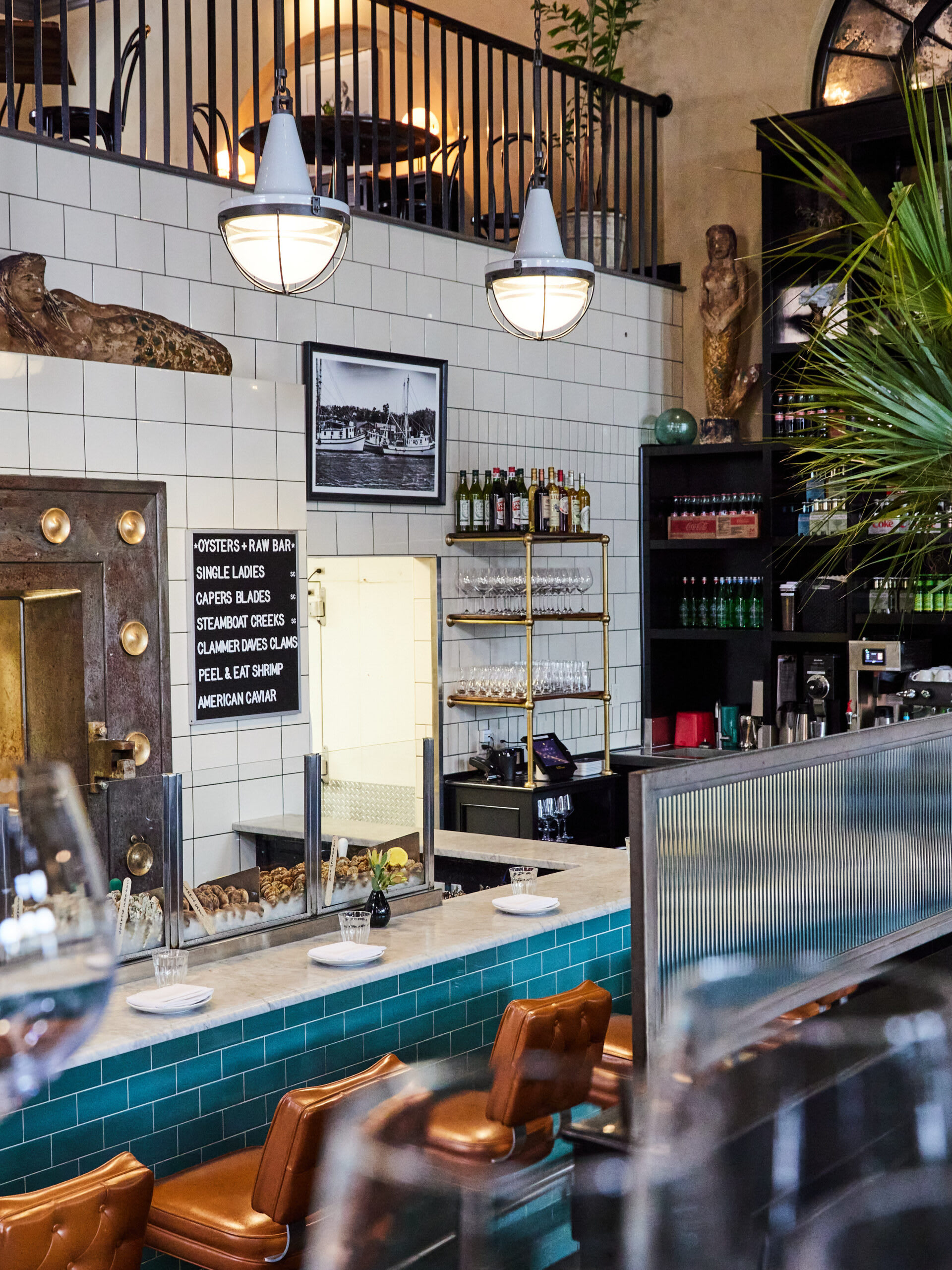 Interior of The Ordinary, a Southern seafood hall and oyster bar, featuring a tiled counter, hanging lights, and a display of fresh oysters.