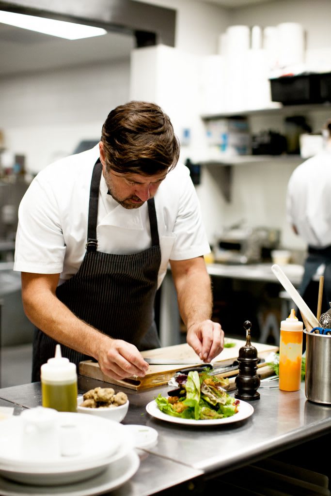 Chef carefully plating a dish with fresh greens and vegetables in a professional kitchen.