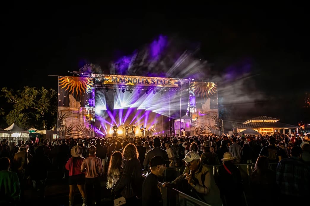 Crowd gathered at night watching a live performance on the Magnolia Stage, illuminated with colorful lights and vibrant visuals.