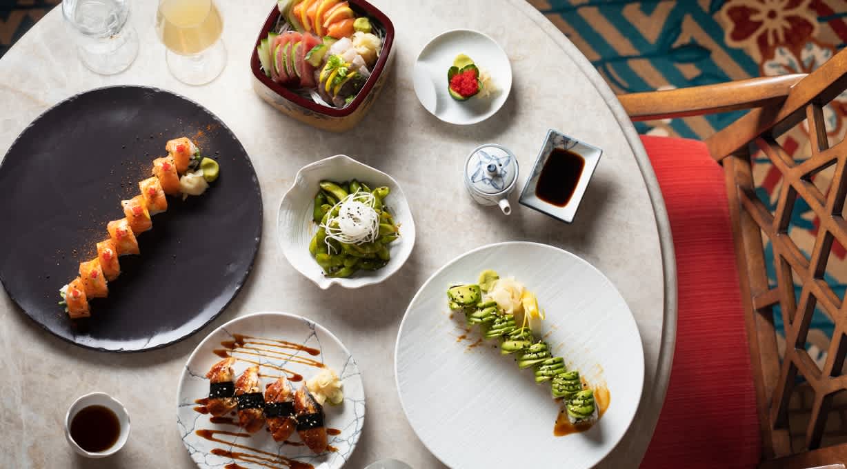 Top-down view of a table set with a variety of sushi rolls, sashimi, edamame, and dipping sauces, ready to be served.