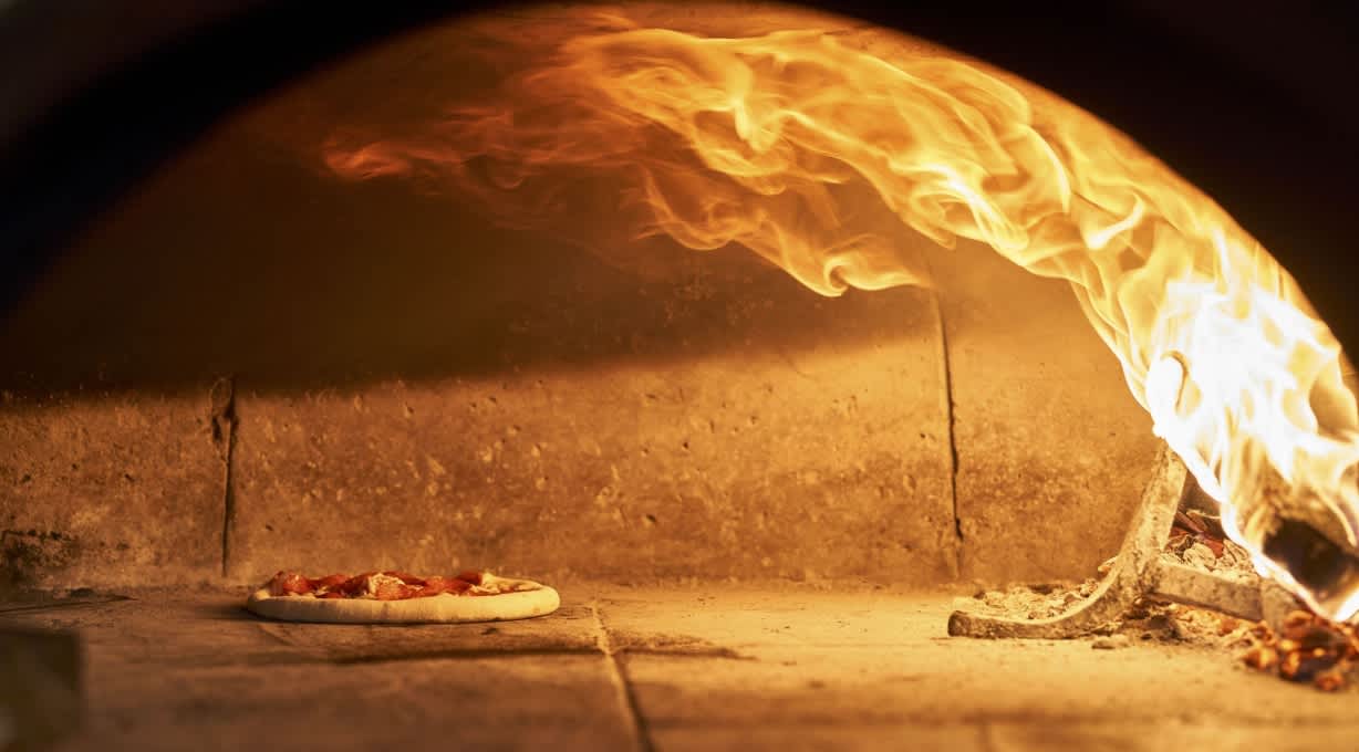 Pizza baking inside a wood-fired oven with bright flames, creating an authentic Italian dining experience at Tavola.