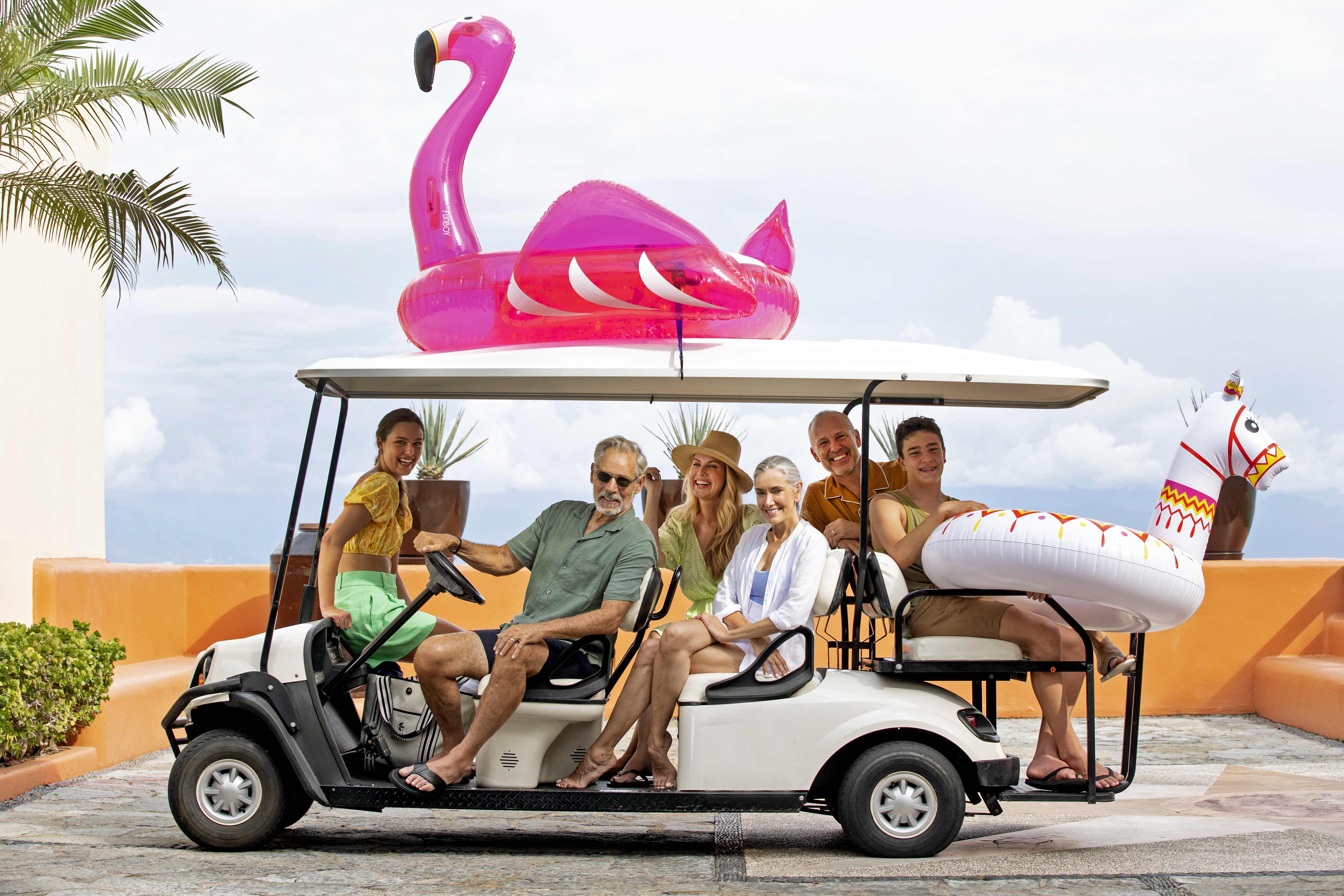 Big family in a golf cart smiling and holding pool floaties.